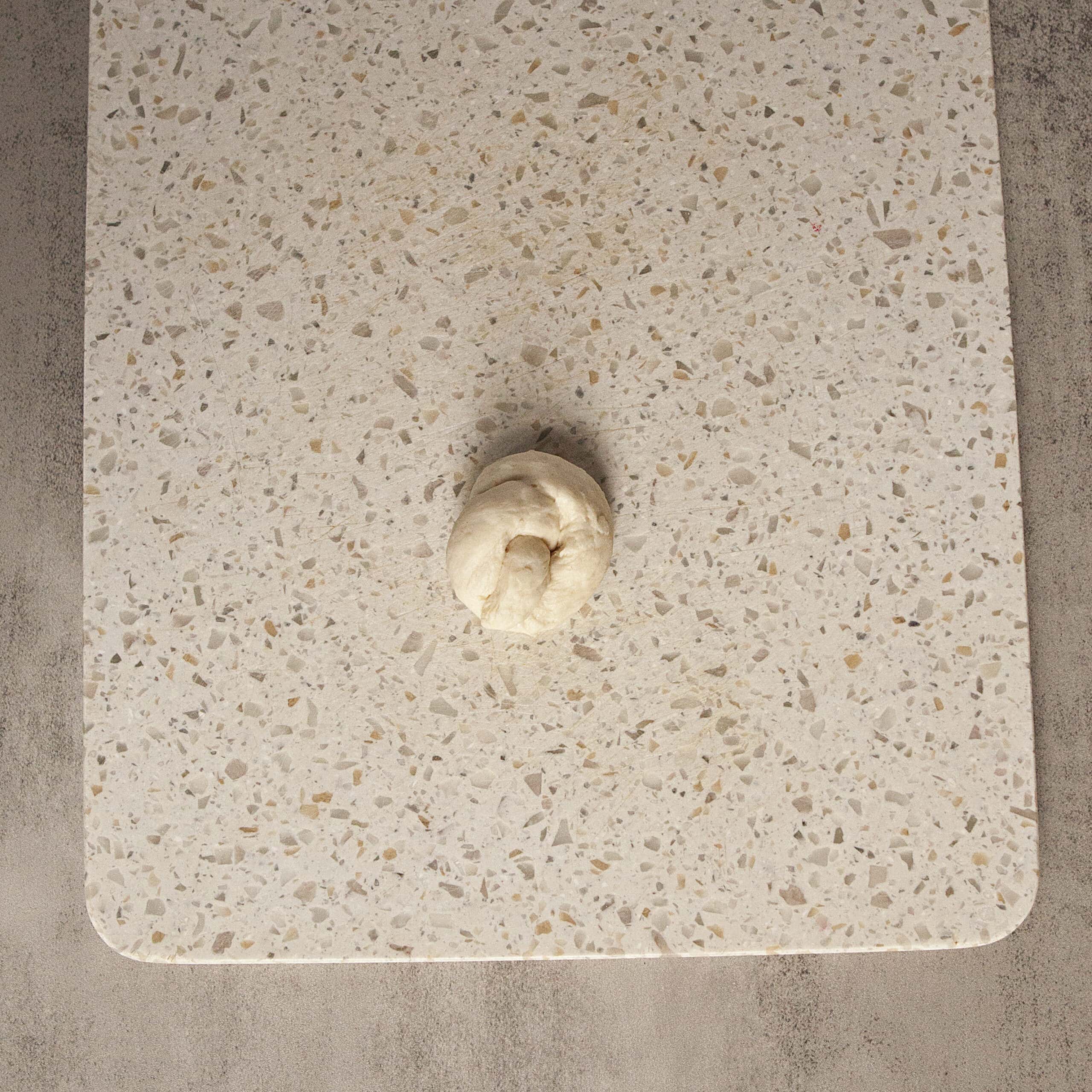 Uncooked garlic knot dough on a white cutting board.