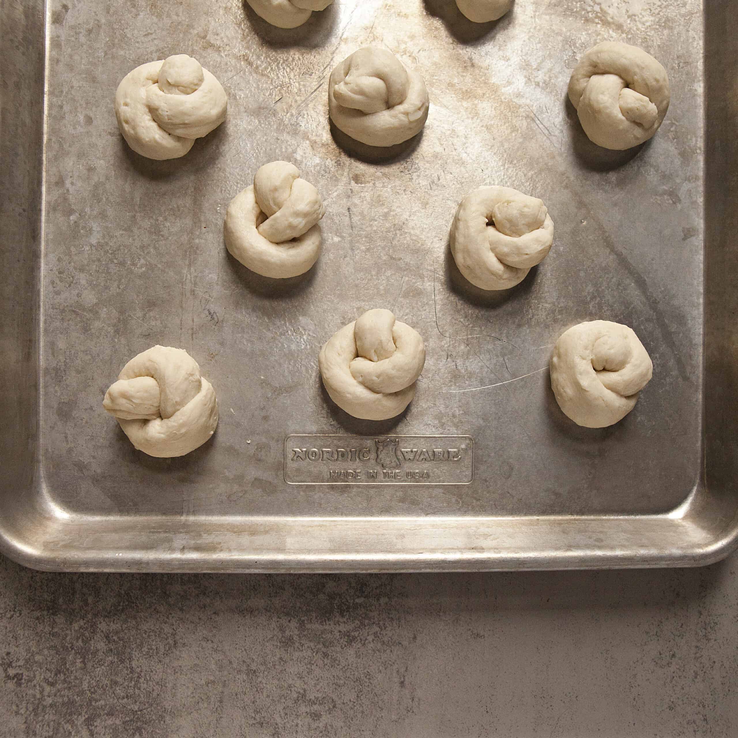 Uncooked garlic knot dough on a silver baking sheet.