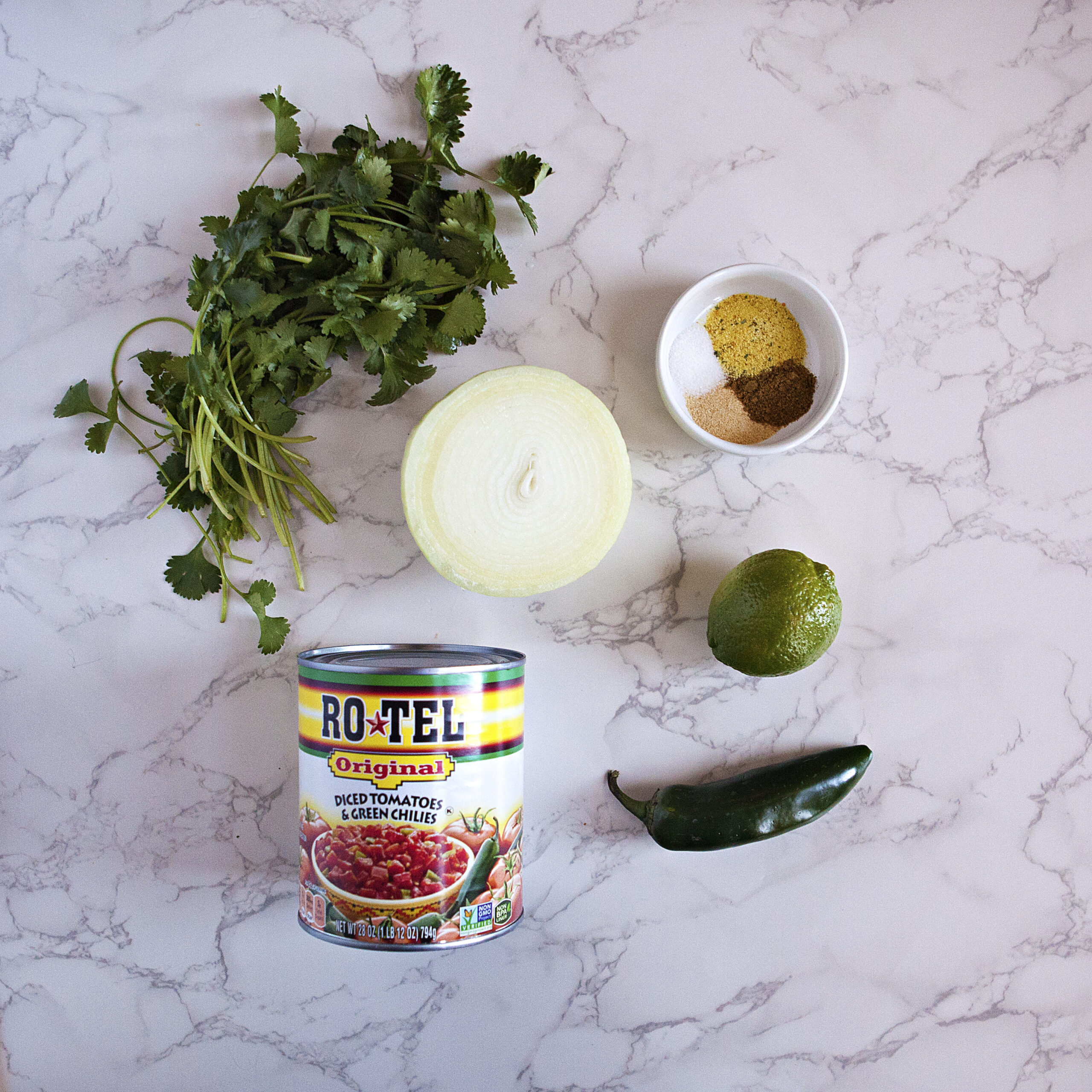 Ingredients for restaurant-style salsa:  A can of Ro-Tel tomatoes with green chilies, yellow onion, lime, jalapeno, cilantro, and a bowl containing garlic powder, salt, cumin, and chicken bouillon powder.