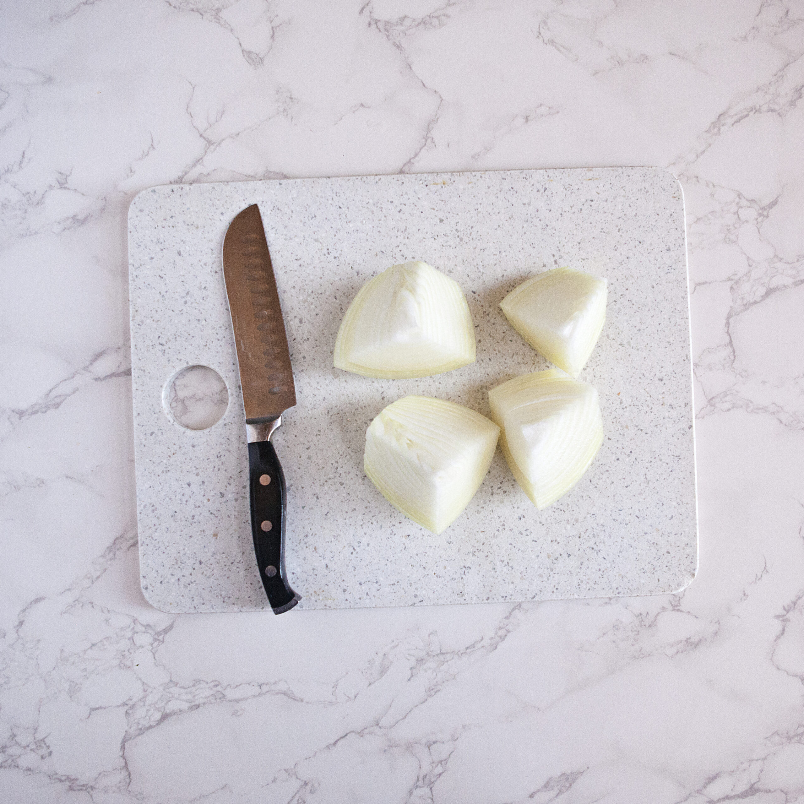 A yellow onion cut into quarters on a white cutting board next to a chef's knife.