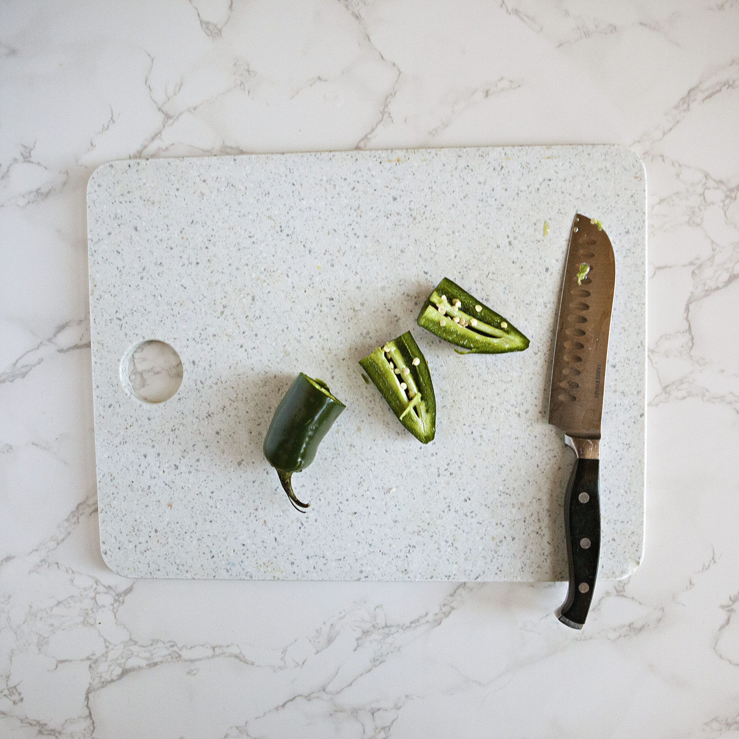 A jalapeno pepper cut into pieces on a white cutting board next to a chef's knife.