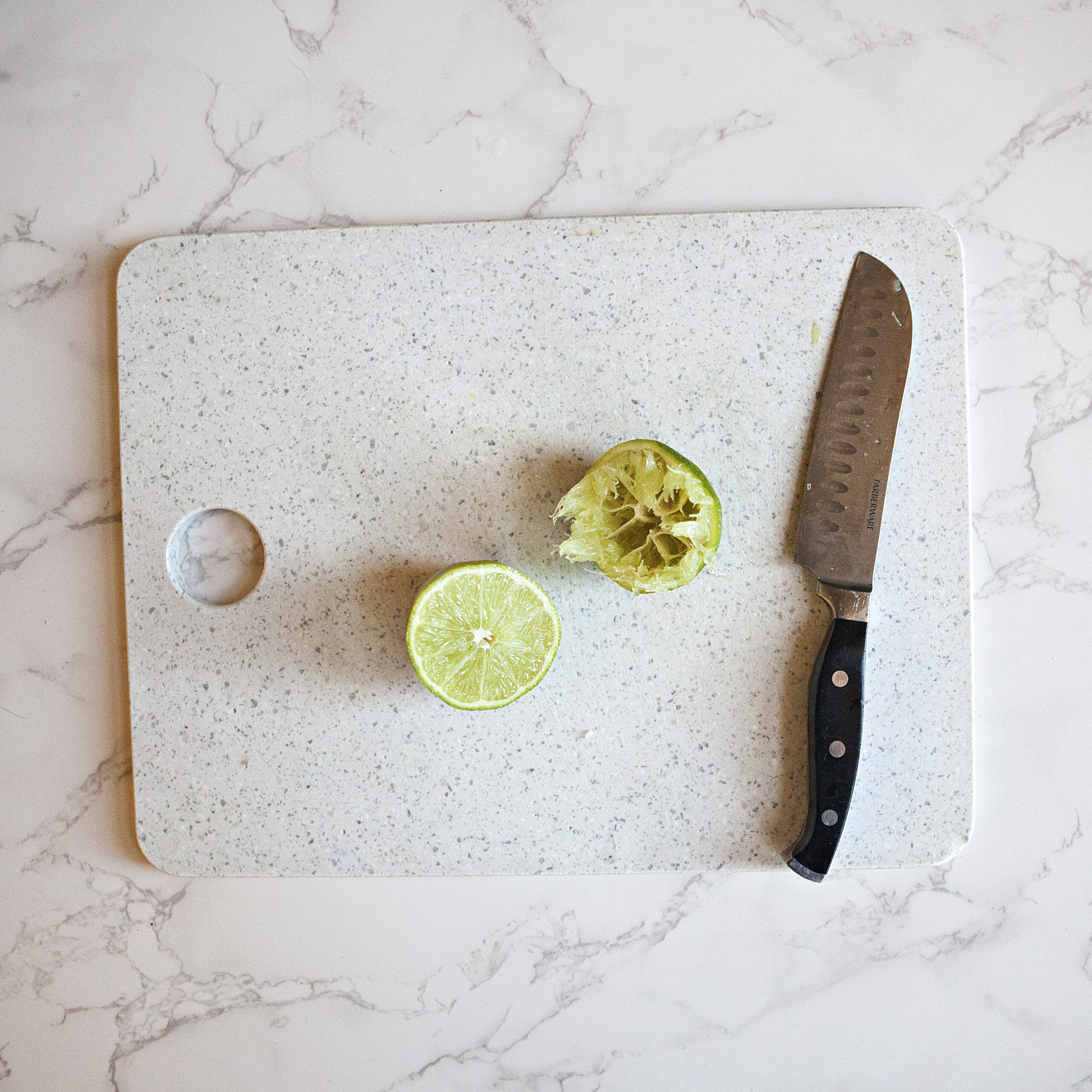 Two halves of a lime on a cutting board next to a chef's knife.  One half has already been juiced.