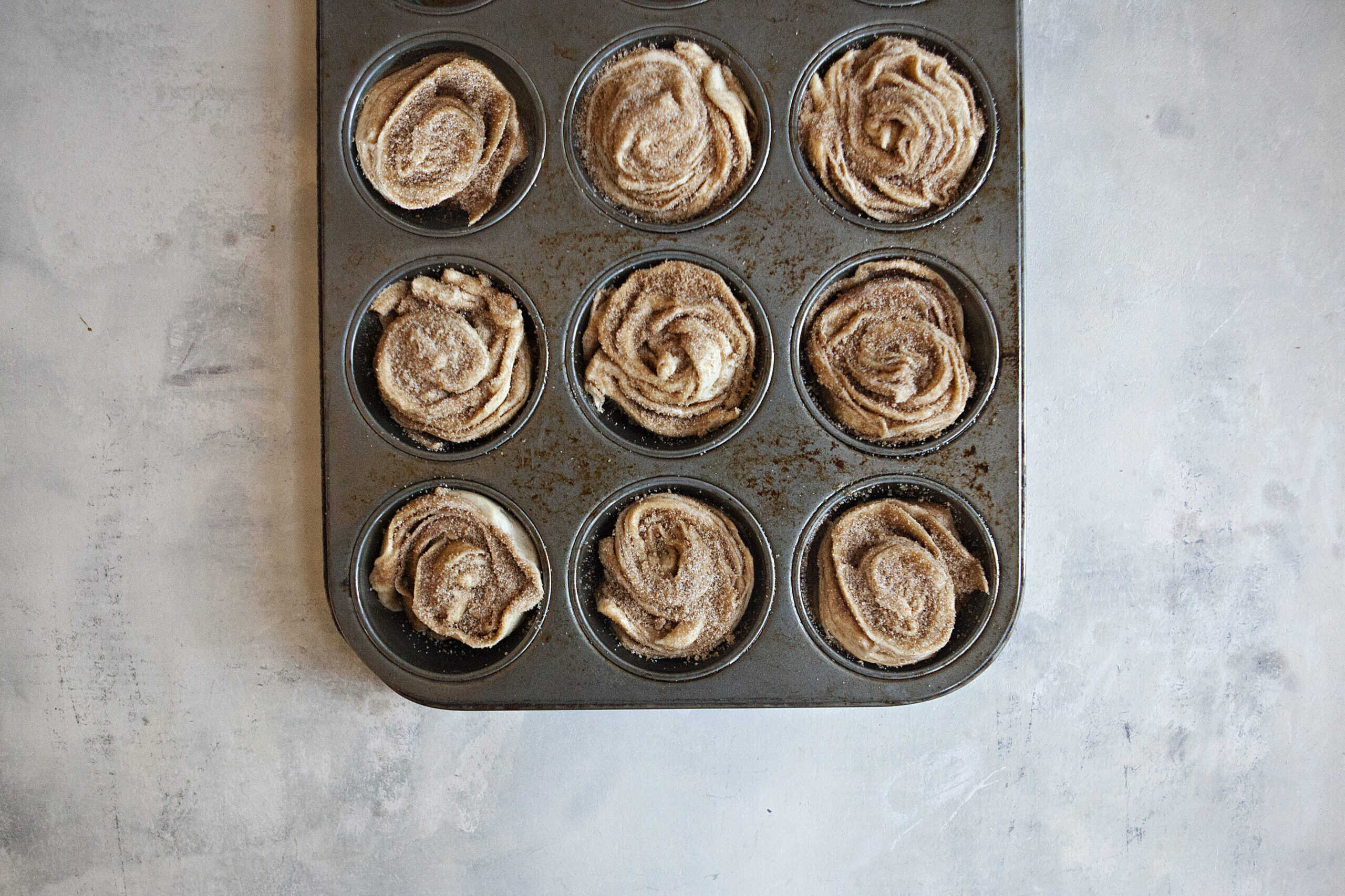 Unbaked cinnamon-sugar cruffins in a muffin tin.