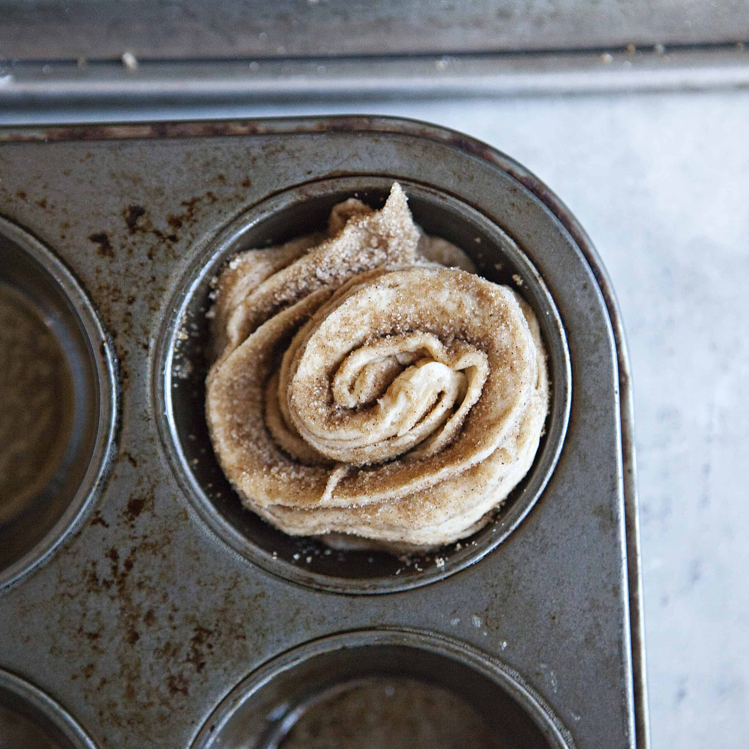 An unbaked cinnamon-sugar cruffin in a muffin tin.