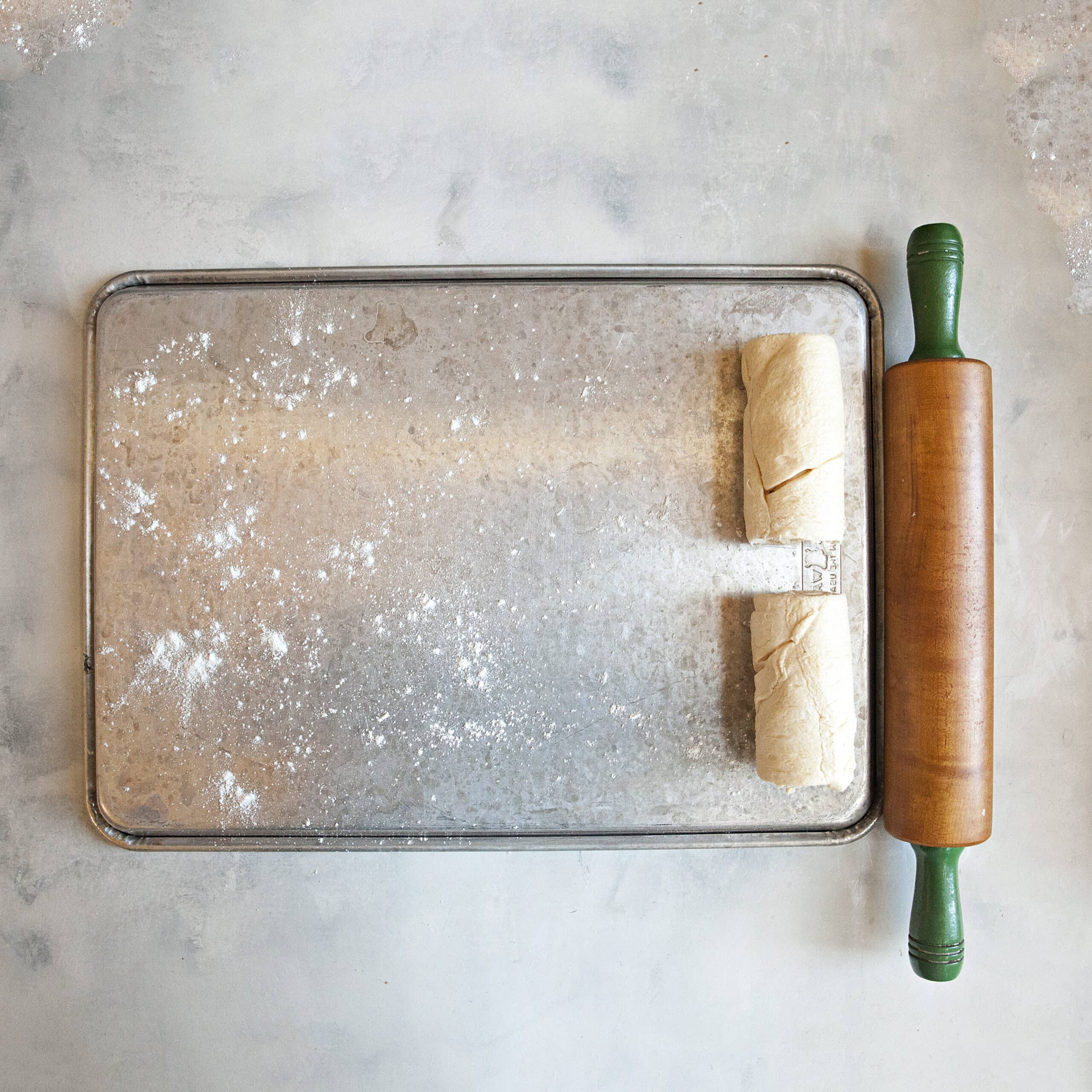 A baking sheet turned over with crescent roll dough placed on top next to a rolling pin.