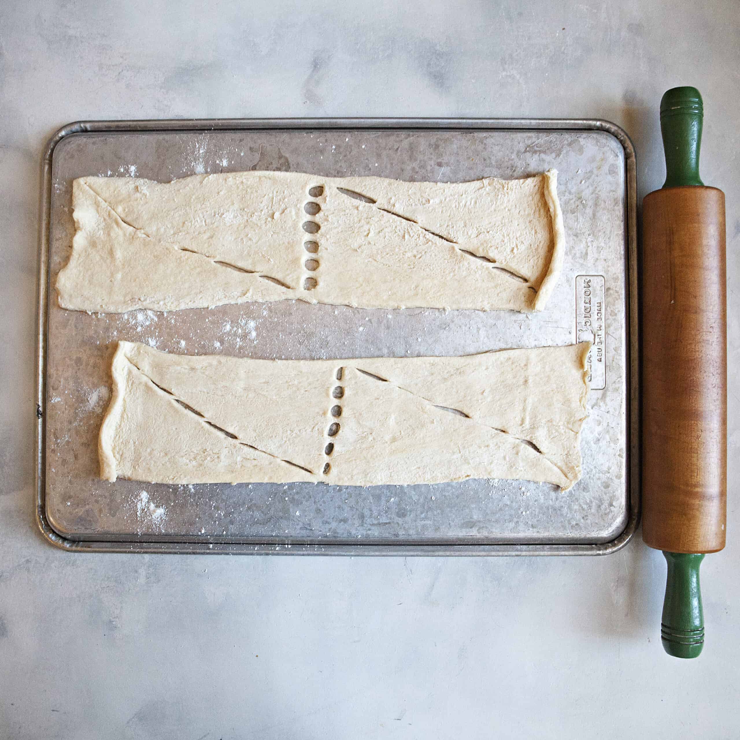 A baking sheet turned over with crescent roll dough placed on top next to a rolling pin.