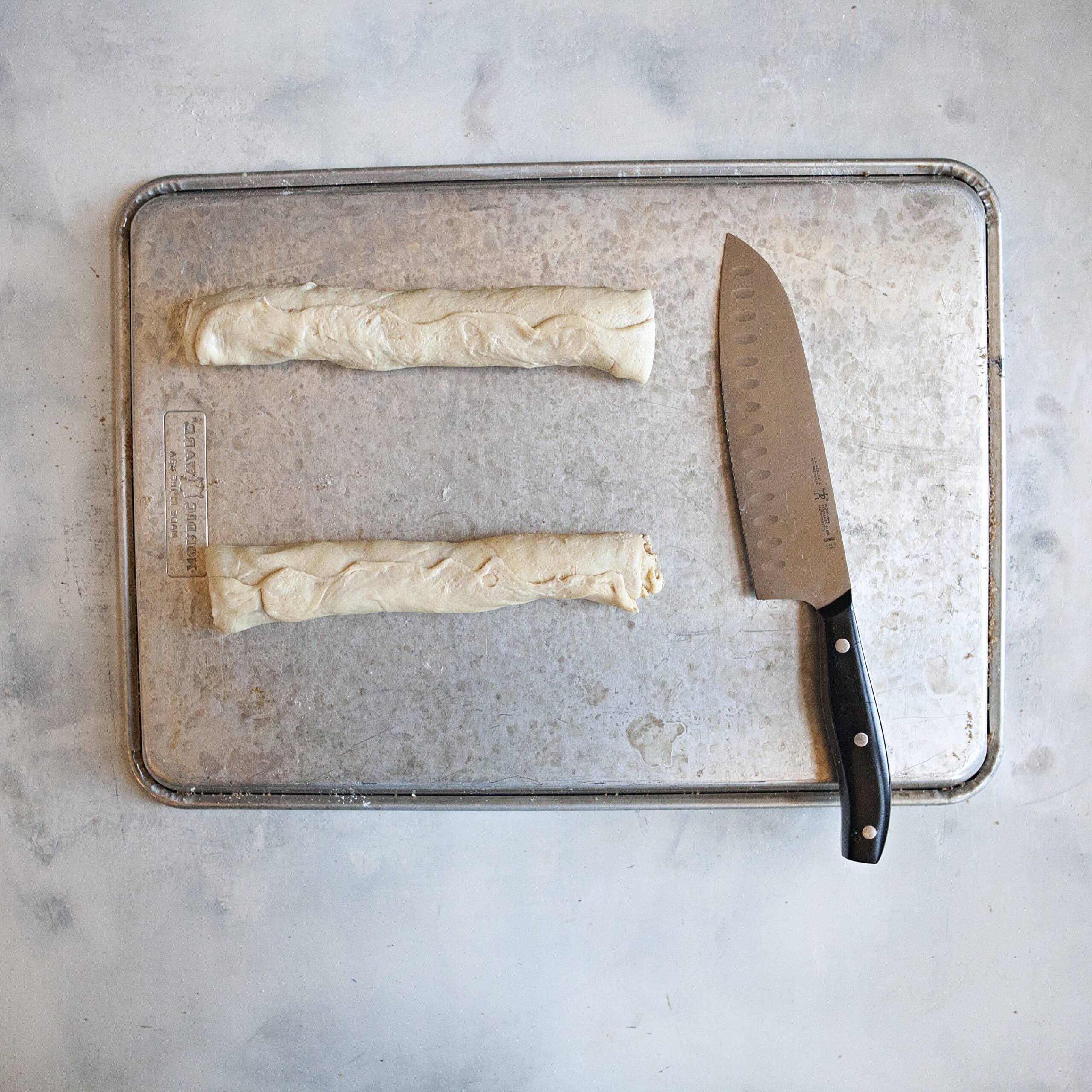 Two cylinders of crescent roll dough on a metal baking sheet with a chef's knife.