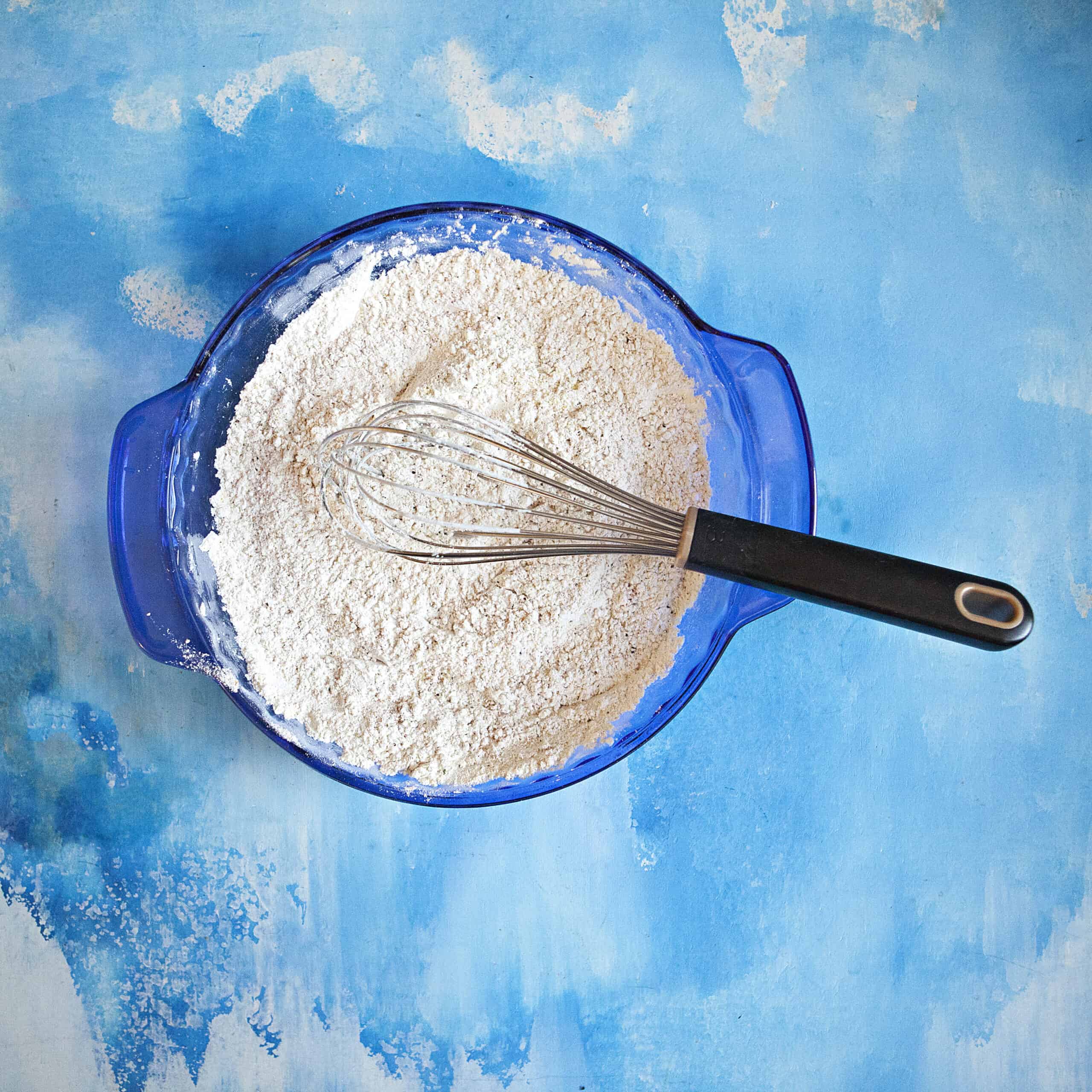 Flour mixture in a blue pie plate with a whisk, on top of a blue backdrop.
